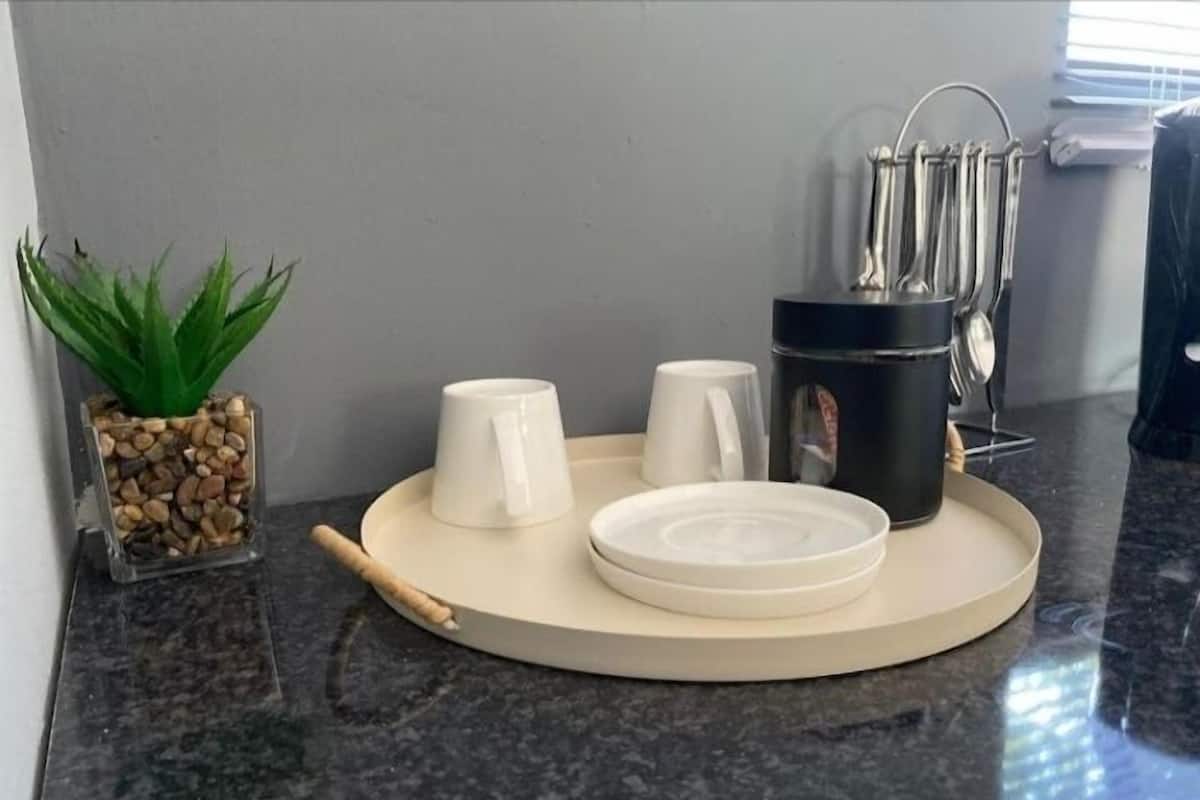 Una encimera de cocina con una bandeja que contiene una cafetera, dos tazas blancas y un plato.
