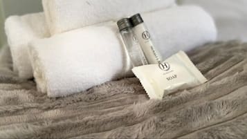 A neatly folded white towel, a bottle of soap, and a soap packet on a textured grey surface.