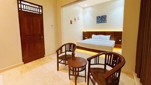 A bedroom with a bed, two wooden chairs, a small table, a door, and a wall with a picture. - Ndalem Singgah Malioboro By Abiza (Yogyakarta)