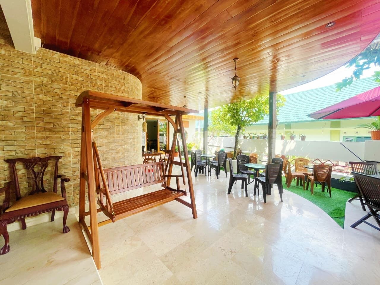 A covered outdoor seating area with a swing set, wooden chairs, and tables.