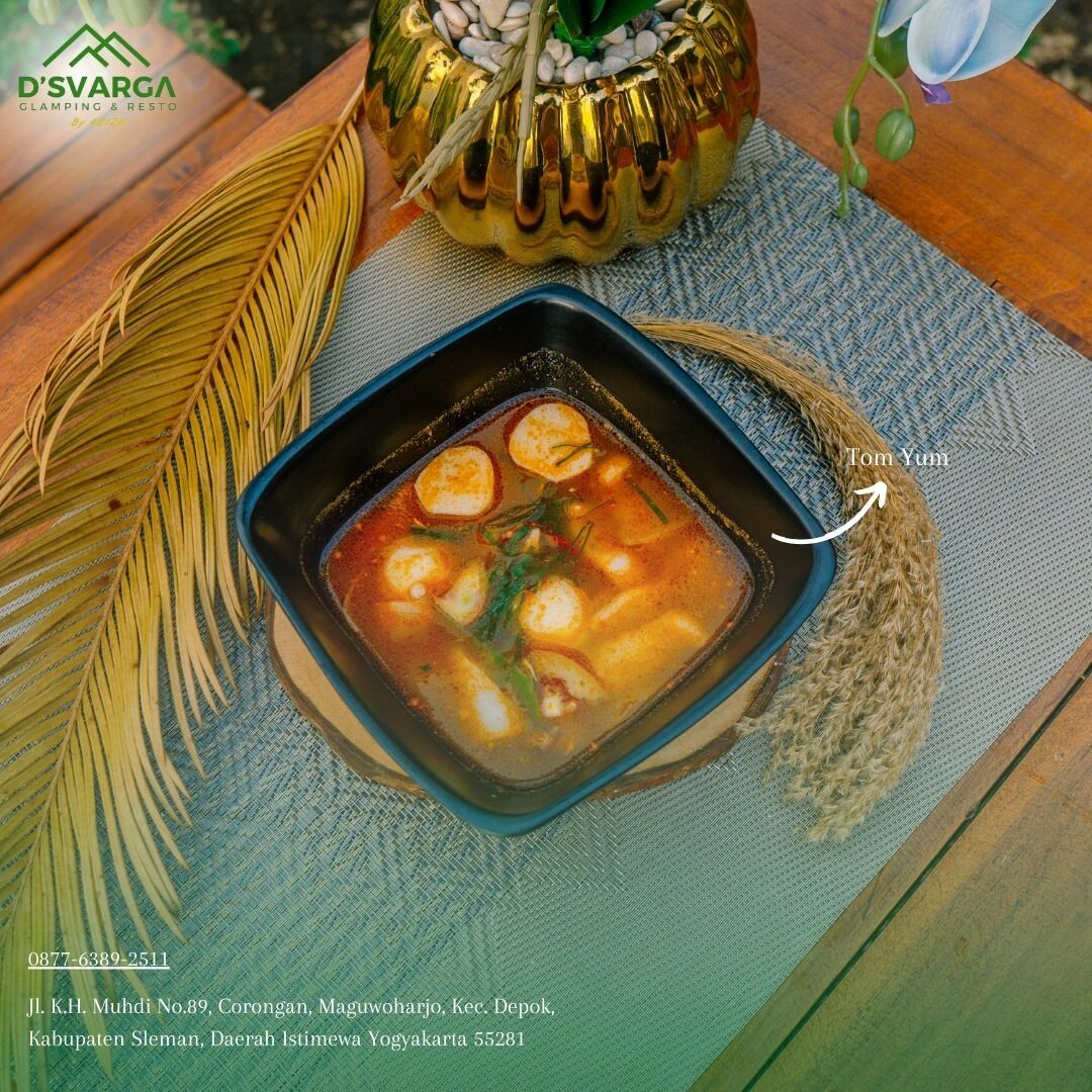 A bowl of Tom Yum soup with a decorative bowl and a palm leaf beside it.