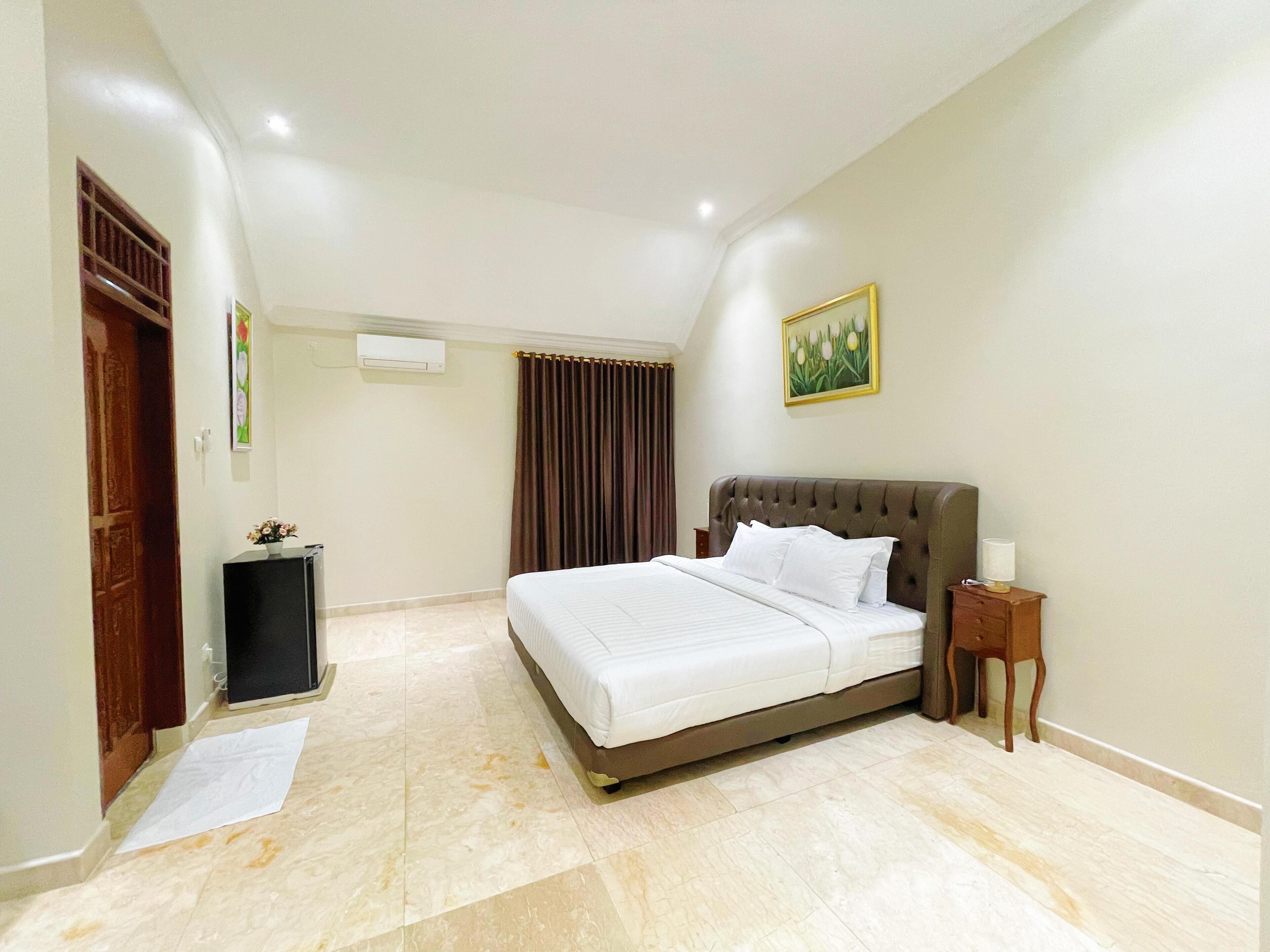 A hotel room with a large bed, a bedside table, a wall-mounted air conditioner, and a painting.