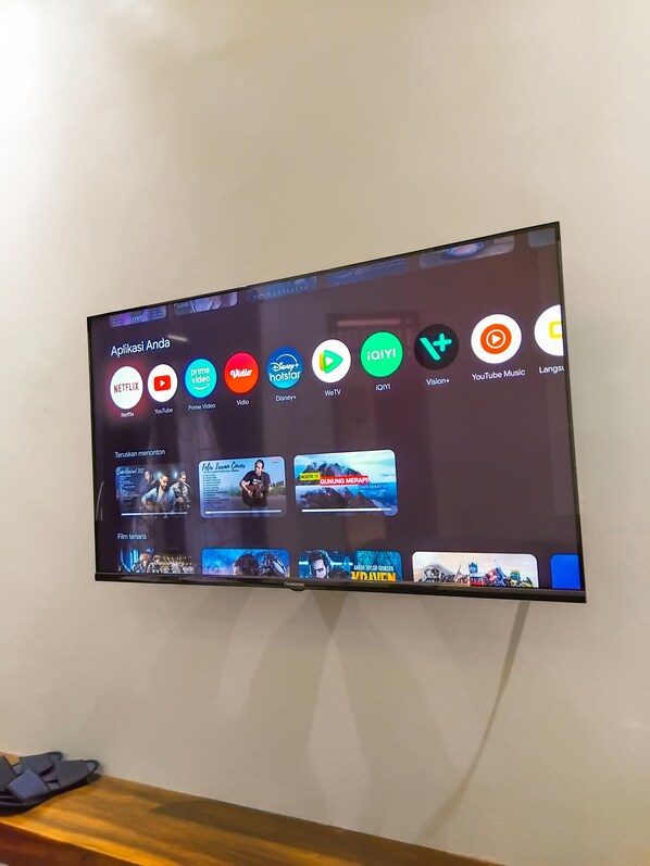 Un téléviseur à écran plat fixé au mur affiche l’interface d’un service de diffusion en continu, avec différentes icônes d’applications.