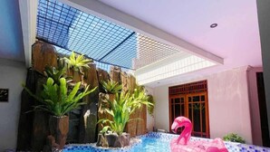 An indoor swimming pool with a pink flamingo float, a rock waterfall feature, and a tiled floor. - Ndalem Singgah Malioboro By Abiza (Yogyakarta)