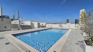 Une piscine sur le toit, avec une terrasse carrelée, des marches menant à un espace détente et une vue sur le panorama urbain.