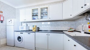 Eine moderne Küche mit weißen Schränken, einer Waschmaschine, einer Kaffeemaschine und einem Spülbecken.