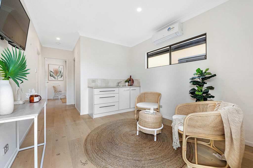 A modern living room with a TV, white cabinets, wicker chairs, a large plant, and a round rug.