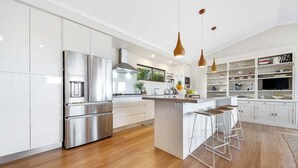 Een moderne keuken met roestvrijstalen apparatuur, een centraal eiland met krukken, hangende verlichting en een wit keukenkastontwerp.