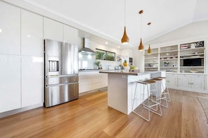 Una cocina moderna con electrodomésticos de acero inoxidable, una isla central con taburetes, iluminación colgante y diseño de armarios blancos.