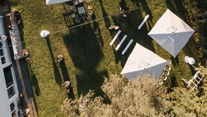An aerial view of a courtyard with multiple white umbrellas and tables, surrounded by greenery and a building. - Feinheit Hotel & Restaurant (Halsenbach)