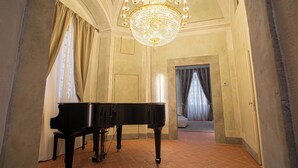 A grand piano in a spacious room with a large chandelier, a tiled floor, and a view into another room with curtains. - Stay in a prestigious place of interest in Florence in the city center (Firenze)
