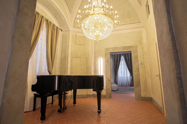 A grand piano in a spacious room with a large chandelier, a tiled floor, and a view into another room with curtains. - Stay in a prestigious place of interest in Florence in the city center (Firenze)
