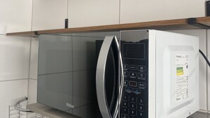 Una cuina moderna amb microones integrat, cafetera i batedora sobre una estant de fusta.