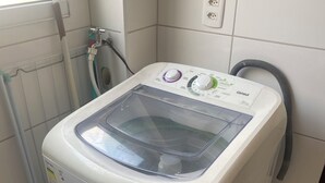 Màquina de rentar amb càrrega frontal, panell de control, presa d'electricitat i una mànega a la paret.
