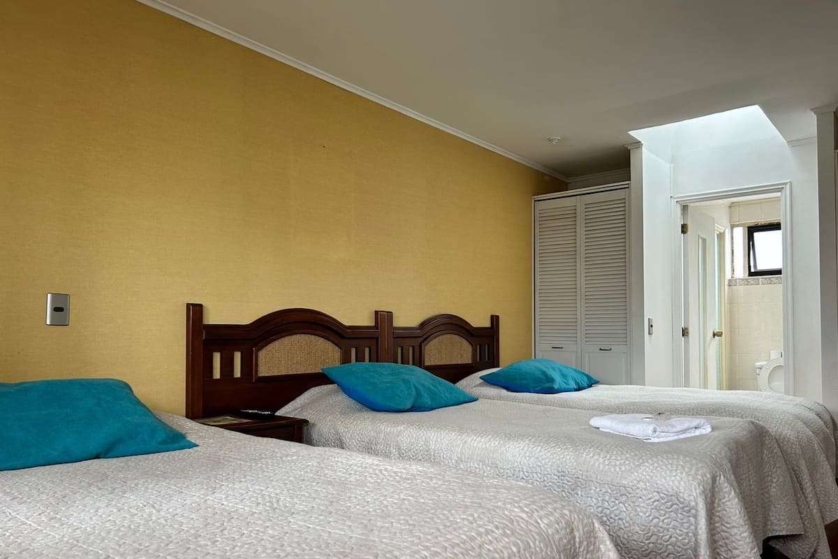 A hotel room with two beds, a wooden headboard, a yellow wall, and a skylight.