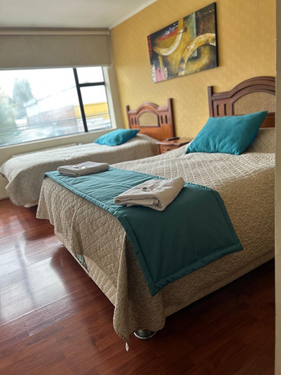 Una camera d'albergo con due letti, testiere in legno e un'ampia finestra.