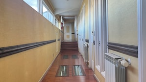 A long, narrow hallway with wooden floors, large windows on one side, and doors on the other. - Hostal Don Guillermo (Natales)