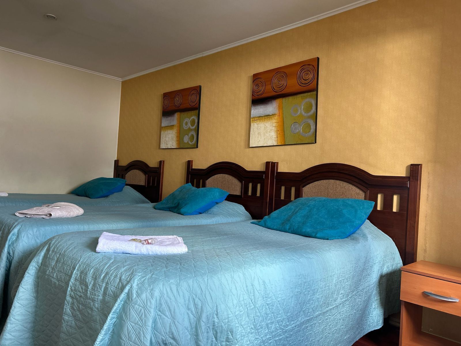 Habitación de hotel con dos camas, cada una con cubrecama y almohadas azules a juego. Dos cuadros decoran la pared sobre las camas.