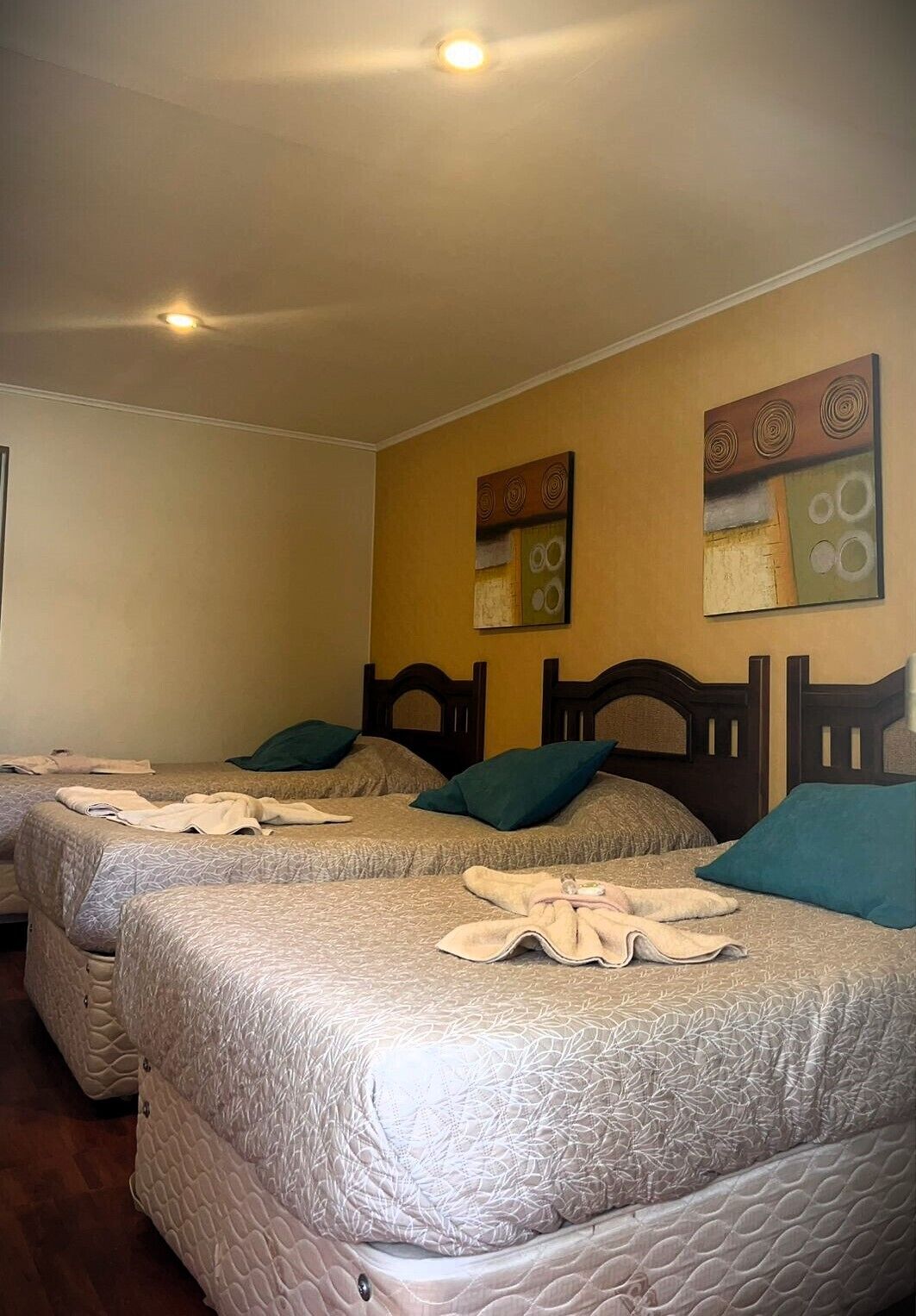 A hotel room with three beds, each with a headboard and pillows. There are two wall art pieces above the beds.