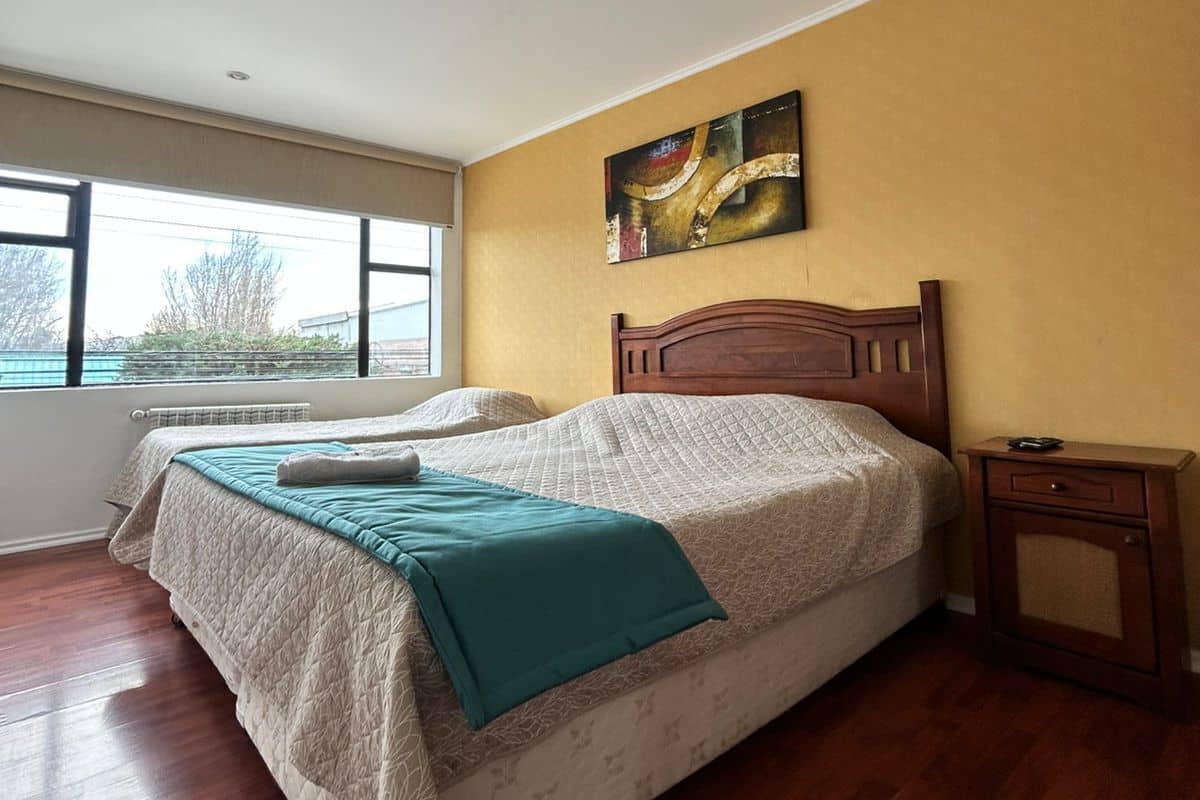 A bedroom with a bed, a nightstand, a window, and a painting on the wall.