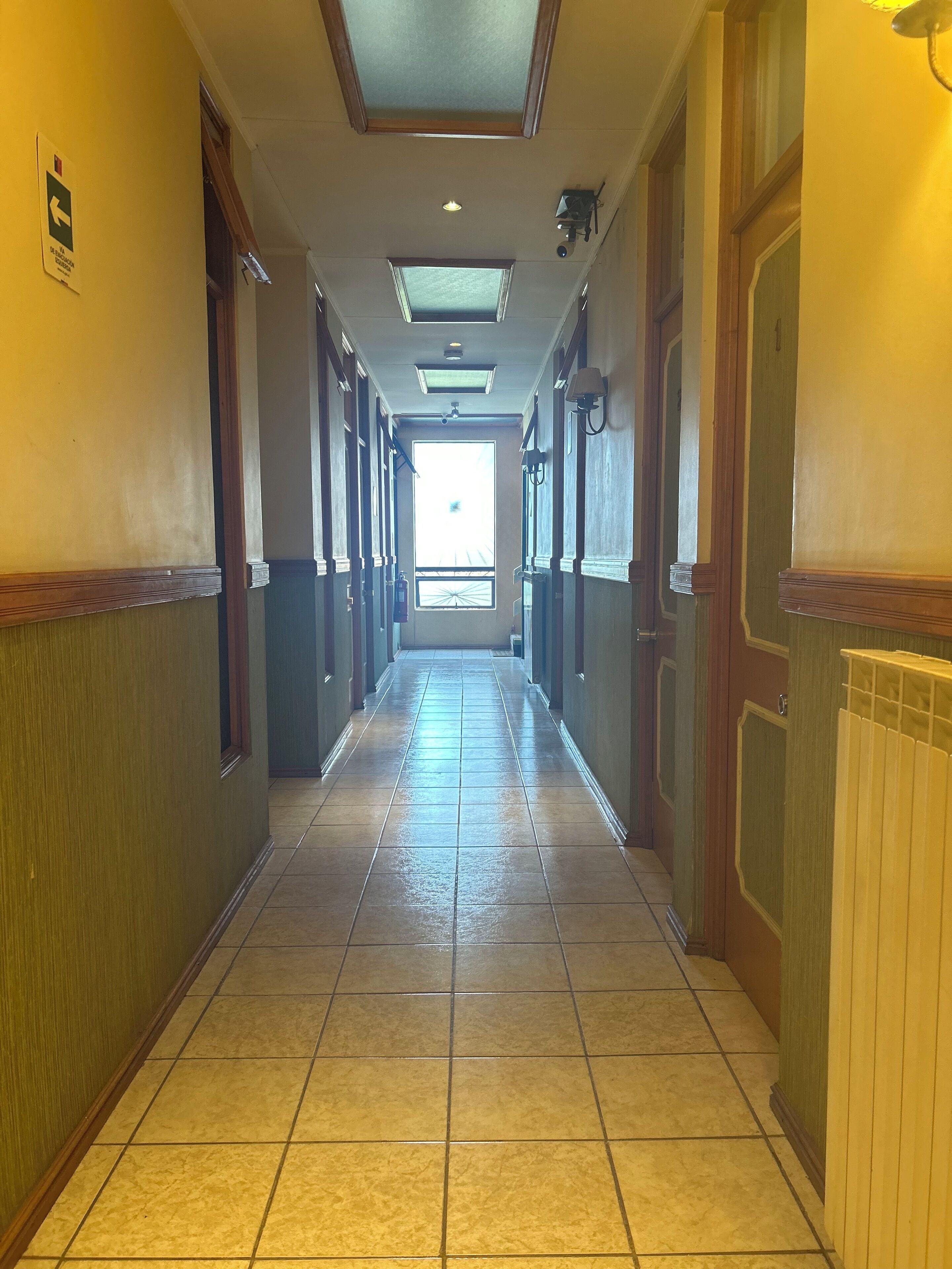 Een lange, smalle gang met betegelde vloer, houten deuren en een plafond met inbouwverlichting.