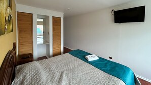 A hotel room with a bed, a television mounted on the wall, and a painting on the wall. - Hostal Don Guillermo (Natales)