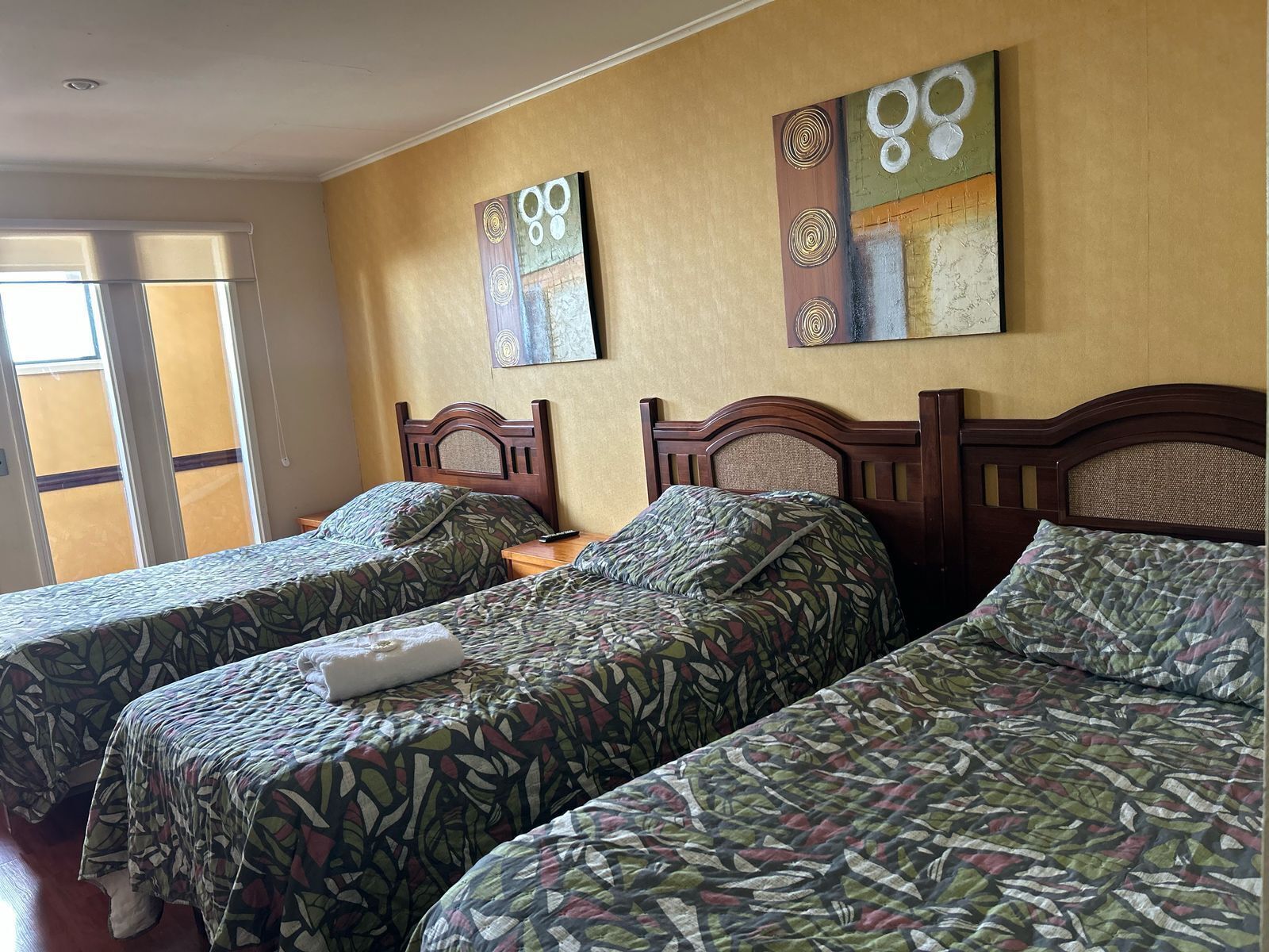 A hotel room with two single beds, a large window, and artwork on the wall.