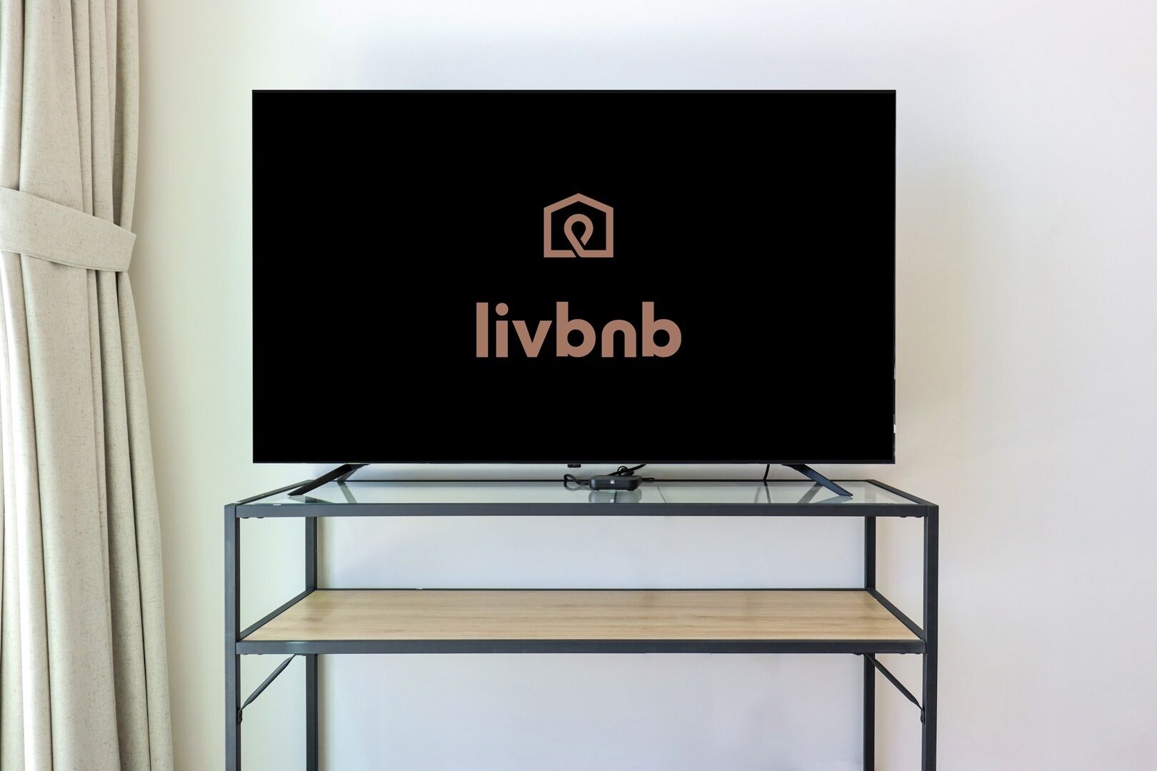 Un téléviseur à écran plat fixé sur un meuble TV moderne en métal noir, doté d’une étagère en bois.