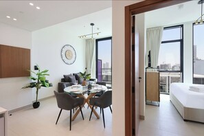 Een moderne hotelkamer met een zithoek, een bed, een groot raam met uitzicht over de stad, en een wandklok.