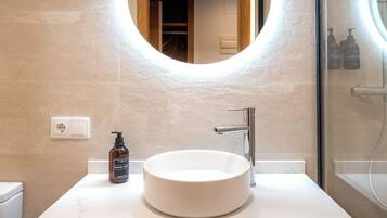 Un bagno con un lavandino rotondo, un rubinetto moderno, un dispenser per sapone e uno specchio con cornice in legno.
