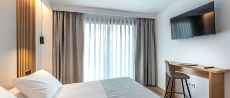 A hotel room with a bed, a desk, a chair, a TV, and a window with curtains.