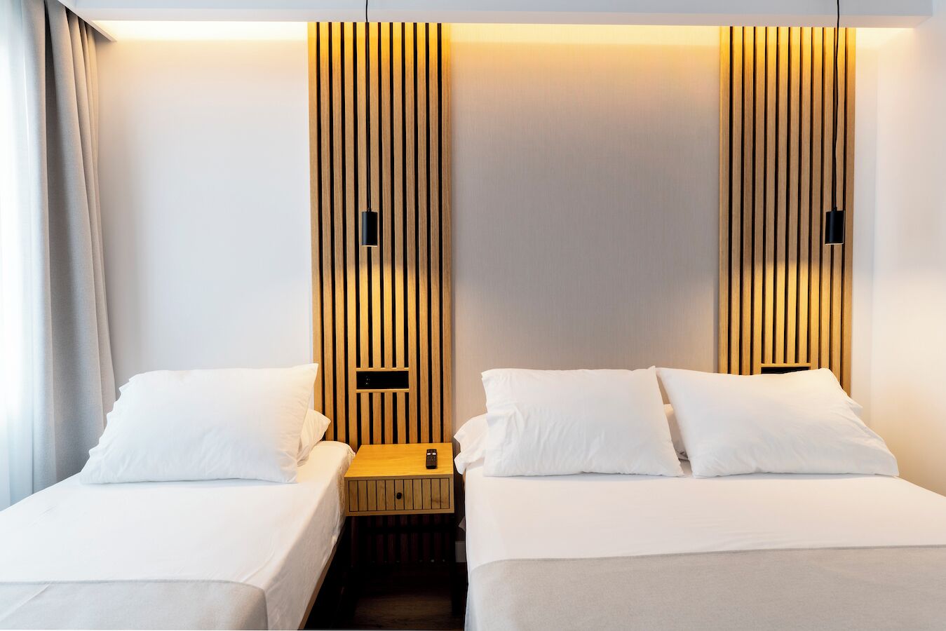 A hotel room with two single beds, a wooden headboard, a small bedside table, and a remote control on the table.