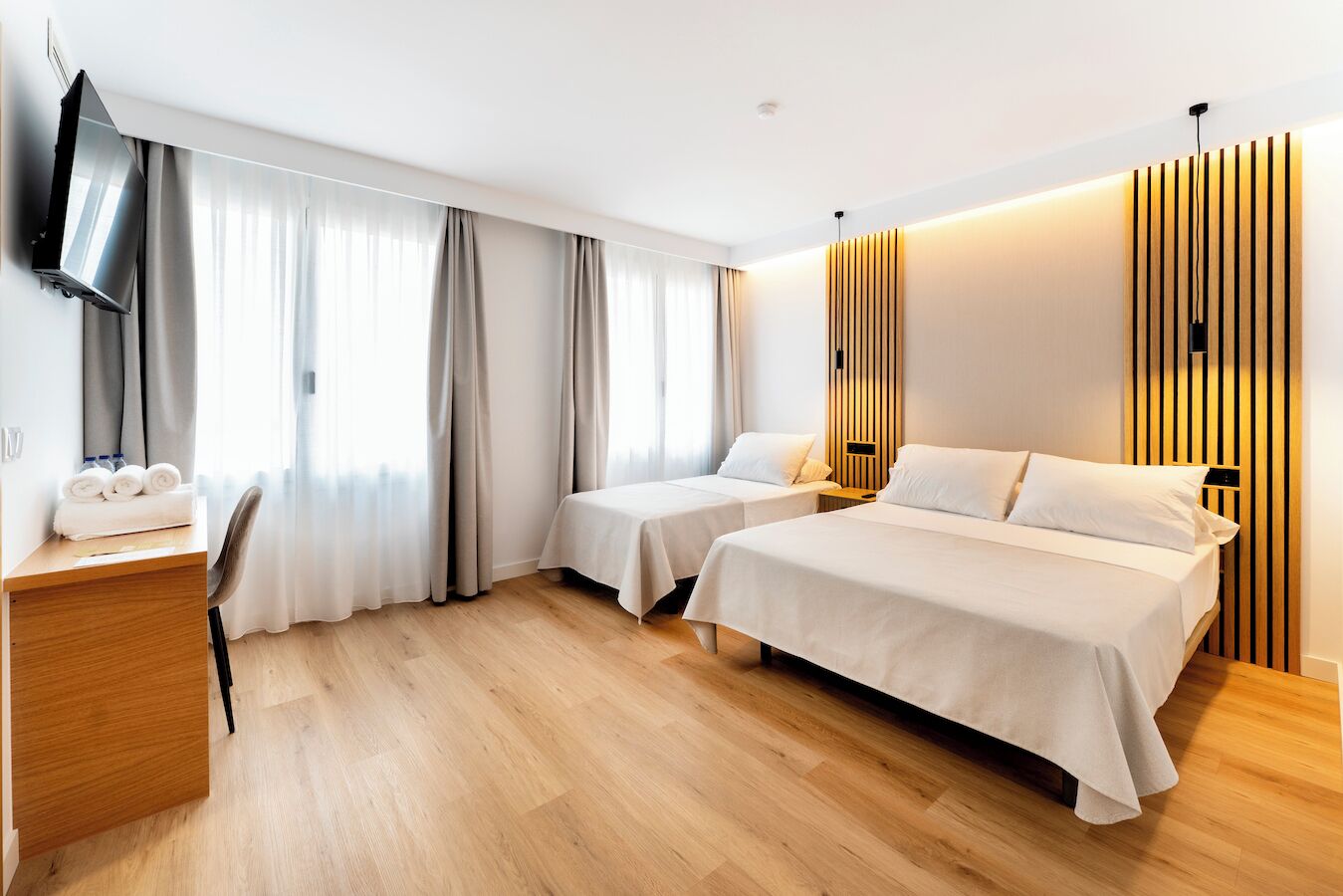 Una habitación de hotel con dos camas, un escritorio, un televisor y un panel de pared de madera.