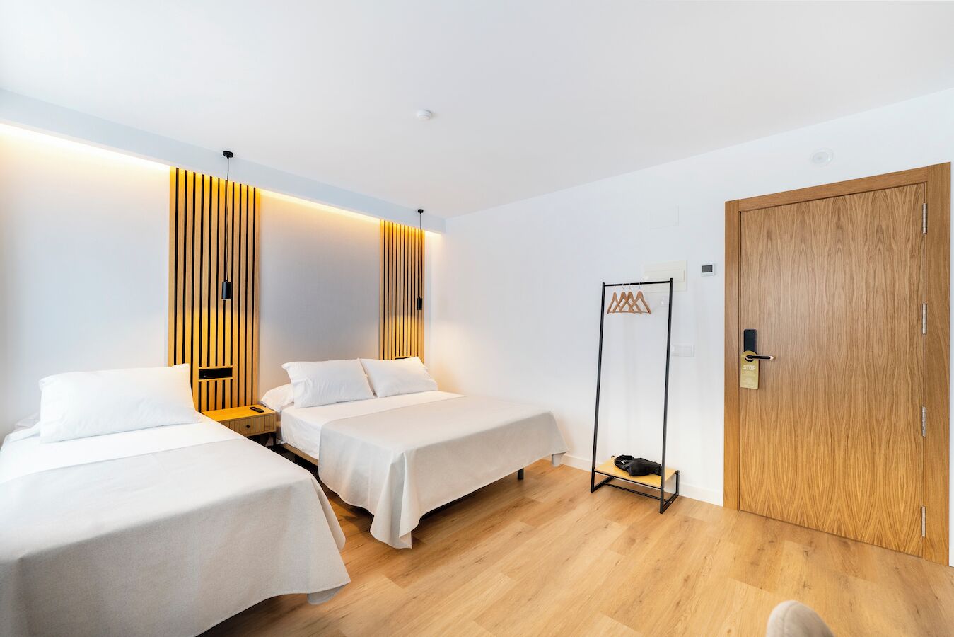 Habitación de hotel con dos camas, un armario de madera, perchero y una puerta con cerradura.