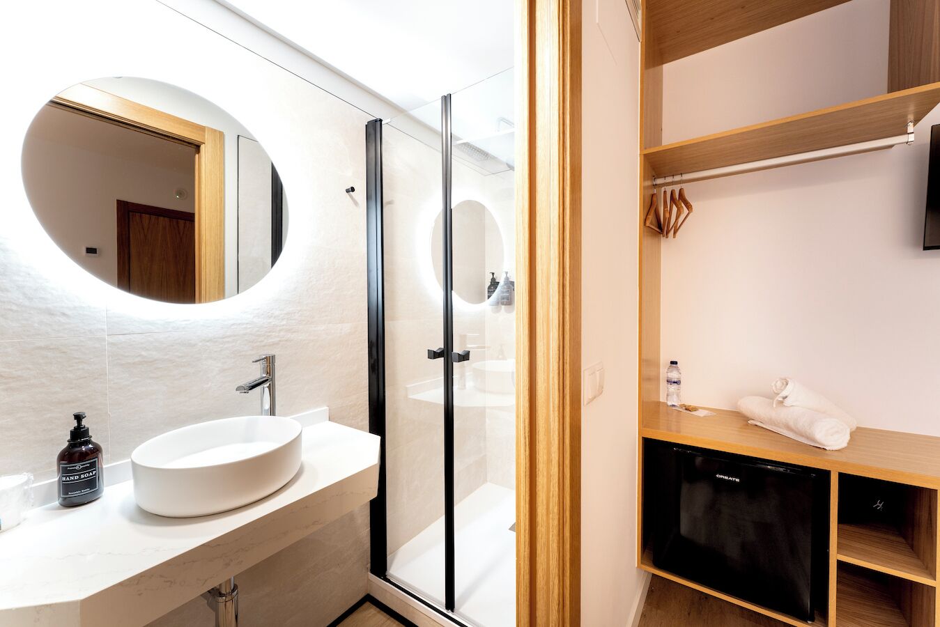 Un baño moderno con un espejo redondo, un lavamanos blanco y una cabina de ducha de cristal.
