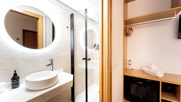 Un baño moderno con un espejo redondo, un lavamanos blanco y una cabina de ducha de cristal.