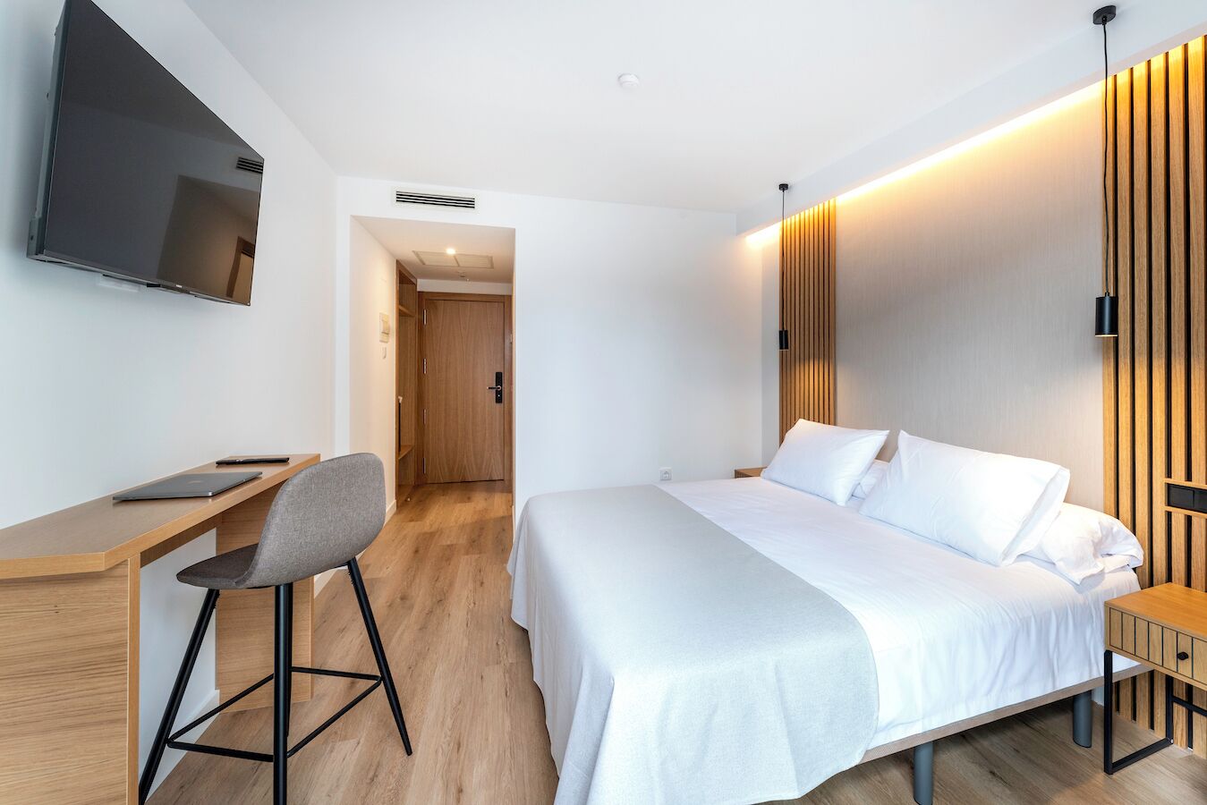 Una habitación de hotel moderna con cama, escritorio, silla y televisor montado en la pared.