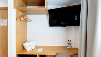 Ein Hotelzimmer mit einem Holztisch, einem Fernseher, einem kleinen Ablagefach mit Handtüchern, einer Wasserflasche und einem schwarzen Gerät.