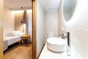 A modern hotel room with a bed, bedside table, and a round white sink with a mirror.
