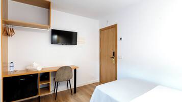 A hotel room with a bed, a desk with a chair, a television, and a wardrobe.