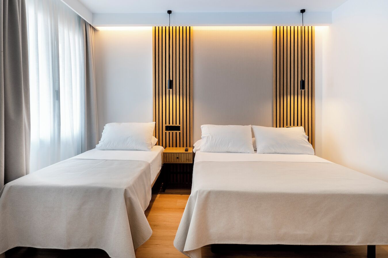 Une chambre d’hôtel avec deux lits simples, un mur recouvert de panneaux en bois et une petite table de chevet avec une lampe.
