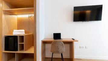 Une pièce comprenant une armoire en bois, un bureau avec un ordinateur portable, une chaise et un téléviseur fixé au mur.