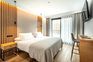 A modern hotel room with a bed, a desk, a chair, and a TV.