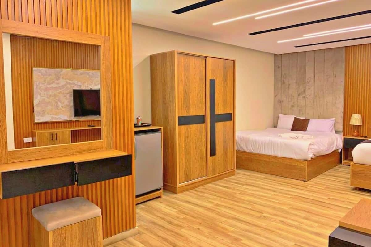 A modern bedroom with a wooden wardrobe, a bed, a small desk, and a mirror.