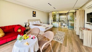 A modern hotel room with a red sofa, a bed, a dining area with a table and chairs, and a bathroom with a bathtub and shower. - Roone Pyramids View Inn (Giza)