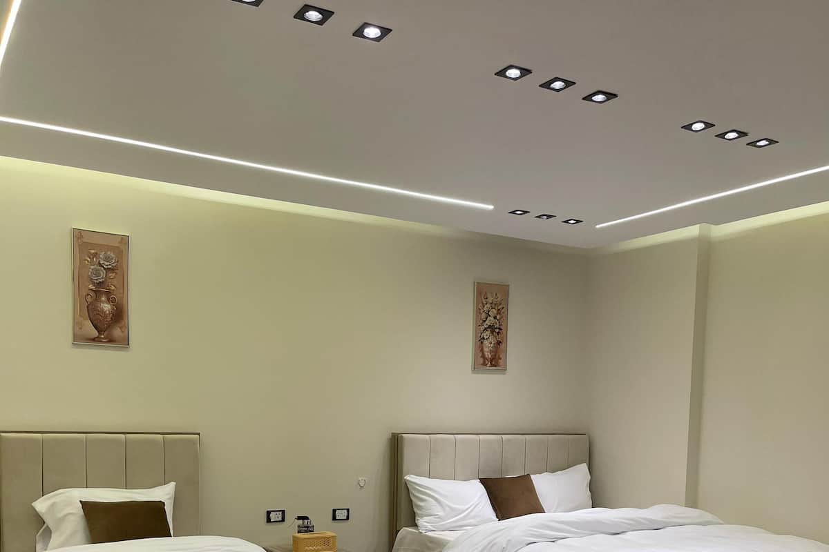 A modern bedroom with two beds, wooden headboards, and a recessed ceiling light fixture.