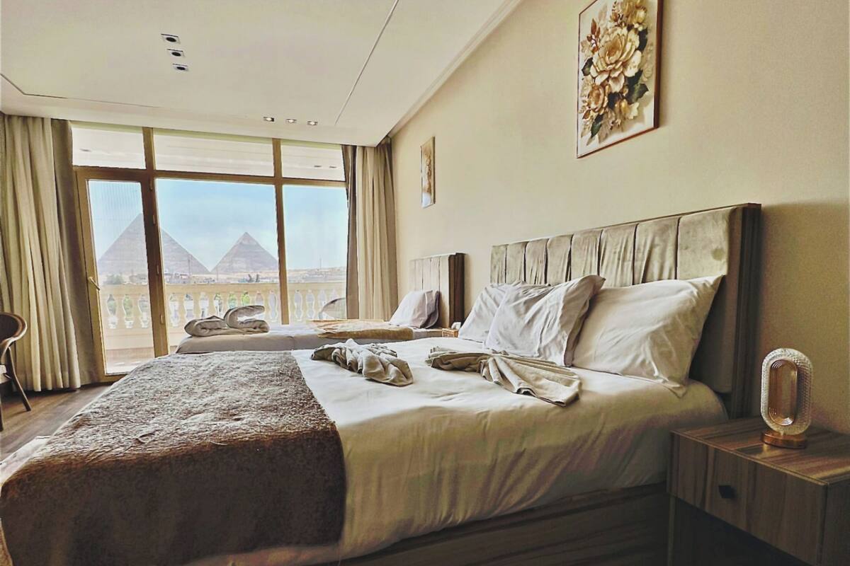 A spacious bedroom with a large bed, a nightstand, and a view of pyramids through the window.