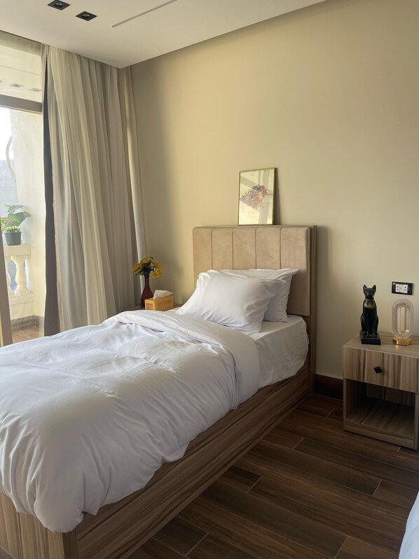 A neatly made bed with white linens, a bedside table with a lamp, a small statue, and a mirror. - Roone Pyramids View Inn (Giza)