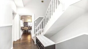 Una escalera con barandilla blanca y piso de madera que conduce a un comedor con sillas y una mesa.