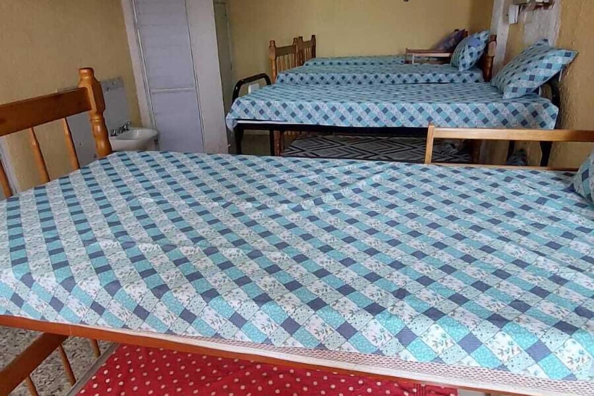A room with two beds, each with a patterned bedspread, a wooden chair, and a small table.